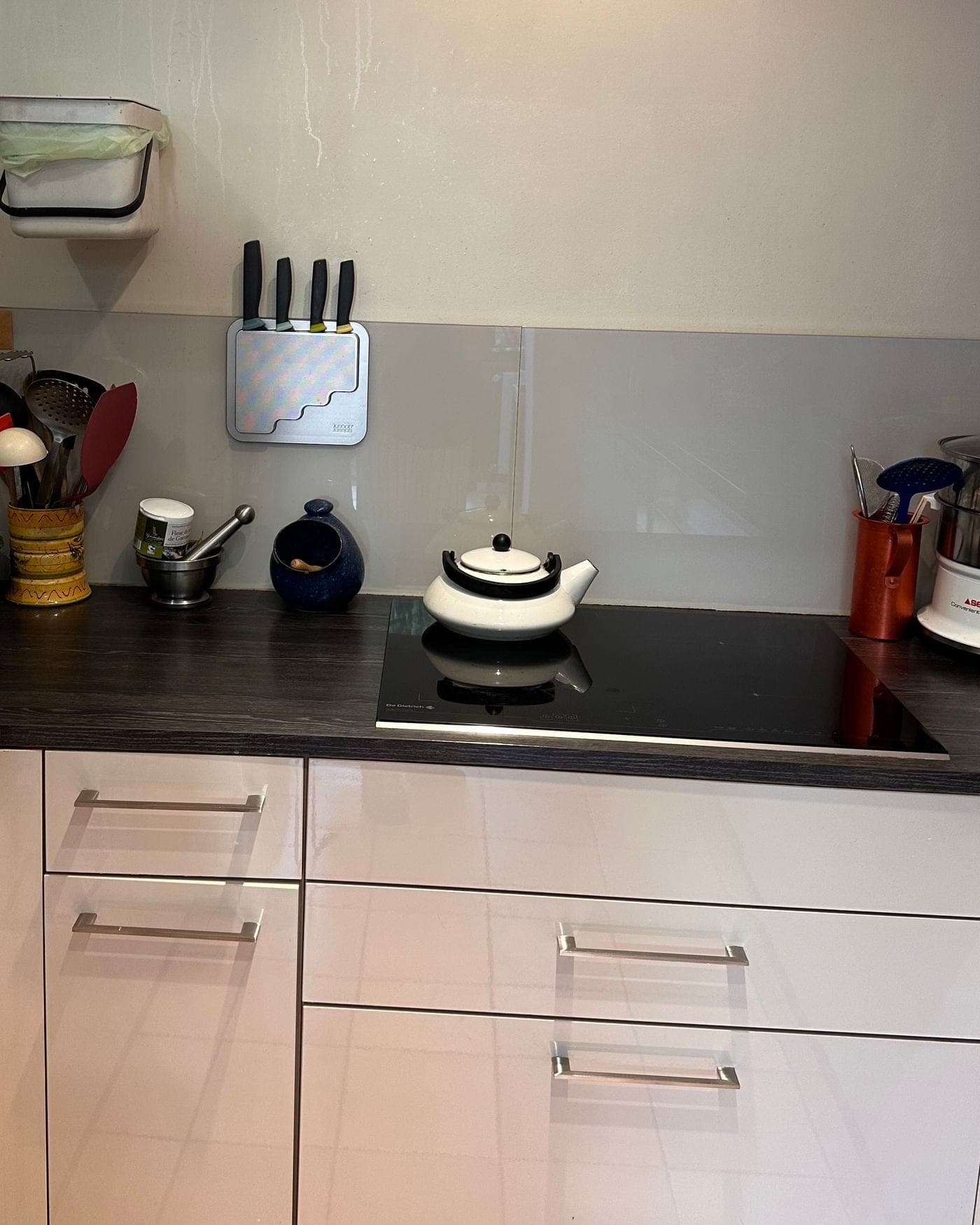 Coin cuisson après le passage : plaque dégagée, bouilloire, porte-couteaux et plan de travail sombre nettoyé